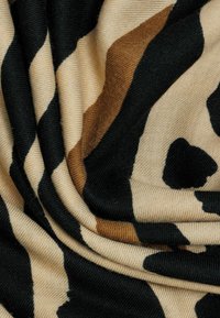 Gewebter Stoff in Beige, Schwarz und Braun mit einem auffälligengrafischen Muster; glatte Textur mit drapierten Falten, die den Farbkontrast zur Geltung bringen.