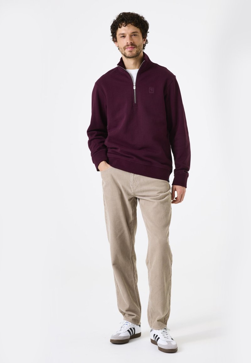 Paarse fleece ritssluiting trui voor mannen met hoge kraag en ribbelmanchetten, gecombineerd met lichtbeige corduroy broek en witte sneakers met zwarte strepen.