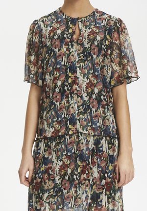 Blusa floreale semi-trasparente con maniche a sbuffo e scollatura a occhio di pernice, caratterizzata da motivi multicolori nelle tonalità di rosso, verde e blu.