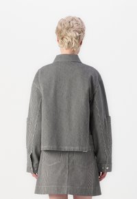 Chaqueta de mezclilla a rayas con mangas largas y un cuello, con un corte corto y bolsillos visibles, en tonos de negro y blanco.
