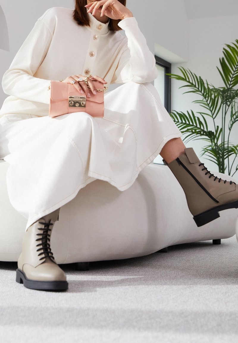 Béžové šněrovací boty s blokovým podpatkem a bočním zipem; nošeny s krémovými šaty s dlouhým rukávem, které mají velké knoflíky, a růžovou kabelkou.