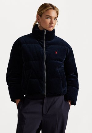 Chaqueta acolchada de pana en color navy con cuello alto, cierre de cremallera y logo rojo en el pecho. Incluye secciones acolchadas y bolsillos laterales.