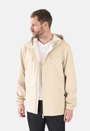 Veste légère beige avec capuche, poignets élastiques, fermeture éclair frontale et deux grandes poches. Texture lisse, design minimaliste.