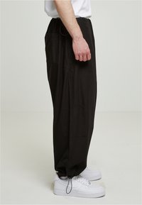 Sorte, letvægtsbukser med en løs pasform og elastisk talje. Har sidelommer og elastiske mansjetter. Bæret med hvide sneakers.