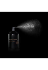 Black bottle with a round shape and a matte finish, featuring gold text reading "Mémoirs d'été," emitting a fine mist from the nozzle.