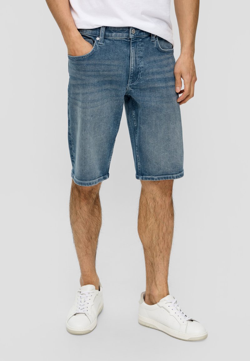 Shorts en denim bleu clair avec un délavage, ourlet roulé et un design à cinq poches classique, associés à des baskets blanches.