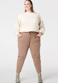 Beige sweatshirt met geplooide, patroonrijke mouwen, gecombineerd met bruin taps toelopende broek met zijzakken. Model draagt slangenleren laarzen.