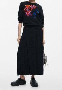 Sudadera negra con bordado floral colorido, combinada con una falda plisada negra y zapatos negros de plataforma cómodos. Bolso sencillo.