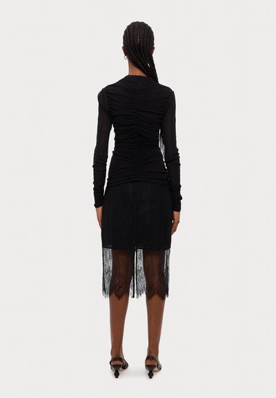 Top negro de manga larga con textura recogida, combinado con una falda negra con borde de encaje y una abertura. Diseño minimalista con detalles transparentes.
