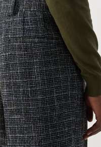 Pantaloni dintr-un amestec de lână, cu un model houndstooth în nuanțe de bleumarin, alb și negru; finisaj texturat; asortați cu un pulover verde.