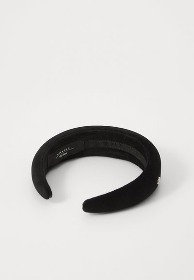 Svart sammetshuvudband med en slät yta, rundade ändar och en subtil logotag på insidan. Mäter cirka 3,8 cm i bredd.