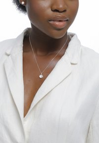 Collier en argent avec un pendentif circulaire en perle, porté sur une chemise en lin blanc, présentant une texture subtile et un détail de col visible.