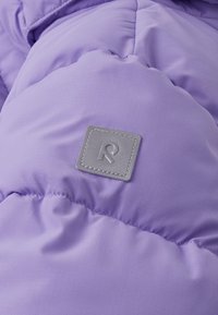 Puffermantel aus hellviolettem Stoff mit gestepptem Muster, ausgestattet mit einem quadratischen grauen Logopatch mit weißer Stickerei.