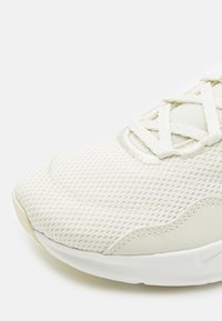 Detailní záběr na off-white sportovní botu s prodyšným síťovaným svrškem, bílými tkaničkami a bílou gumovou podrážkou na jednobarevném pozadí.