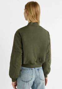 Olijfgroene bomberjack met een geribde zoom, brede mouwen en een gladde textuur. Voorzien van een detail met een zijzak.