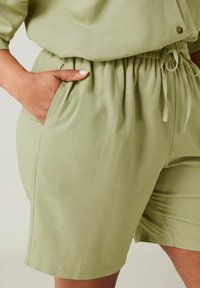Vaaleanvihreät sortit pehmeästä kankaasta, joissa on joustava vyötärö ja nyöri sekä sivutaskut. Sileä pinta ja rento muotoilu.