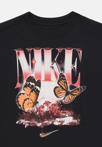 Camiseta negra con gran texto "NIKE" en rojo, dos mariposas naranjas, flores rojas y un logo de swoosh de Nike en plata.