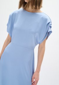 Abito azzurro chiaro realizzato in tessuto testurizzato, con scollatura rotonda e maniche delicatamente arricciate, vita aderente e gonna fluida.