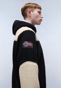 Czarna i beżowa polarowa kurtka z kapturem, bocznymi kieszeniami na zamek oraz naszywką z norweską flagą na lewym rękawie.