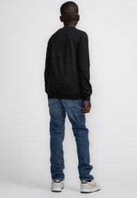Donkergrijze trui met lange mouwen en een ronde halslijn, gecombineerd met lichtblauwe spijkerbroek en witte sneakers met beige accenten.