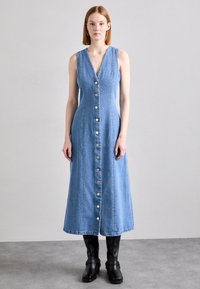 Denimimekko, jossa on V-pääntie, olkaimeton muotoilu, nappikiinnitys edessä ja midimittainen helma. Vaalea sininen väri ja sileä pinta. Mustat nilkkurit.