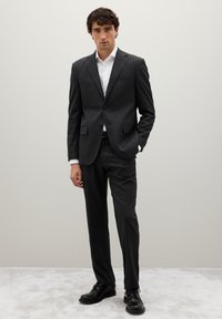 Traje de rayas en carbón con un blazer ajustado y pantalones a juego, combinado con una camisa blanca y zapatos negros de cordones. Textura de tela suave.