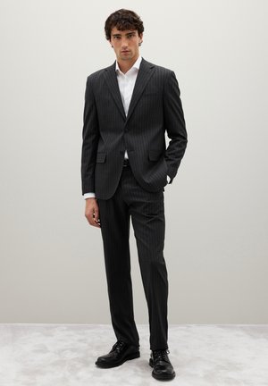Grau gestreifter Anzug mit tailliertem Blazer und passenden Hosen, kombiniert mit einem weißen Hemd und schwarzen Schnürschuhen. Glatte Stofftextur.