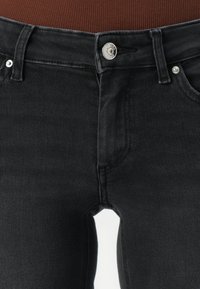 Close-up van de taille van zwarte denim jeans met metalen knoop en riemlussen, gecombineerd met een bruin ribbel top.