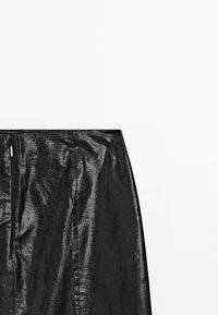 Jupe noire avec une finition métallique texturée. Présente une silhouette droite et une fermeture éclair à l'arrière. Design minimaliste.