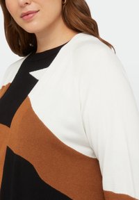 Cardigan in maglia con design a blocchi di colore, con sezioni bianche, nere e marroni. Tessuto morbido e vestibilità rilassata con scollatura rotonda.