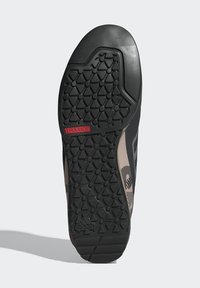 Potplat cipele s crnim trokutastim uzorkom, crvenom oznakom "TRAXION" i utisnutim Adidas logoom blizu pete.