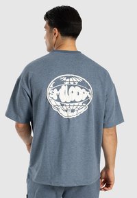 Blå kortærmet t-shirt med et stort hvidt grafik på ryggen, der viser en globe støttet af hænder. Blødt, tekstureret stof.