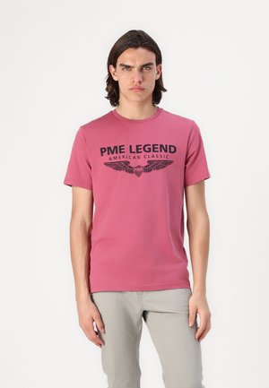 Majica kratkih rukava, kružnog izreza, od ružičaste tkanine. Sadrži crni ispisani tekst "PME LEGEND AMERICAN CLASSIC" s grafikom krila.