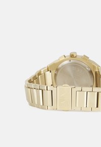 Goldfarbene Uhr mit Metallarmband, das rechteckige Glieder aufweist, einem glatten Gehäuseboden und einer polierten Oberfläche, die ein graviertes Logo zeigt.