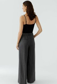 Camisole noire à bretelles réglables associé à un pantalon large à taille haute gris à rayures fines avec poches arrière et tissu texturé.