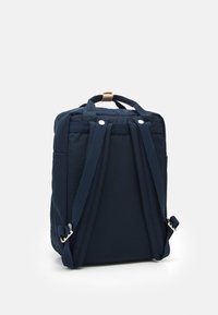 Mochila azul marino con tela acolchada, correas ajustables, asa superior y herrajes plateados. Textura suave con un diseño minimalista.