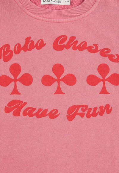 Felpa rosa con testo rosso che recita "Bobo Choses" e "Divertiti", con accenti a forma di trifoglio al centro e colletto a coste.