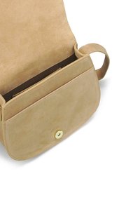Bolso cruzado de ante en tono beige con solapa plegable, que cuenta con un cierre a presión dorado y una única correa. El interior incluye un pequeño bolsillo.