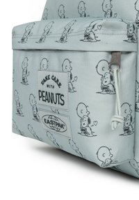 Ljusblå väska med svartvita tecknade figurer från Peanuts. Inkluderar etikett med "Take Care" och Eastpak-logotyp. Hållbart tyg, dragkedjestängning.