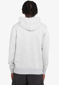 Sudadera gris claro con capucha ajustable, puños y dobladillo en canalé, hecha de una tela suave. Presenta una textura lisa, sin patrones visibles.