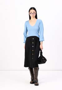 Suéter de malha canelada azul claro com decote em V, saia midi preta de botão, botas castanhas até ao joelho e uma bolsa preta decorada.