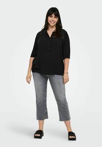 Blusa nera con bottoni e maniche larghe, abbinata a jeans grigi a vita alta. La modella indossa sandali neri a scivolo. Tessuto morbido con dettagli sottili.