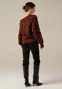 Maglione oversize lavorato a maglia in ruggine con motivo testurizzato, abbinato a pantaloni neri a vita alta e stivali neri lucidi fino al ginocchio.