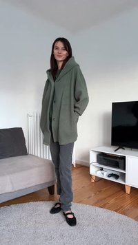 Übergroße grüne Fleecejacke mit großem Kragen und Knöpfen, kombiniert mit grauer Hose und schwarzen Schuhen. Strukturierter Stoff und lässige Passform.