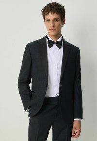 Smoking nero con un motivo a trama, colletti in satin e papillon abbinato su una camicia bianca. Design aderente con una silhouette slim.