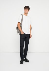 Camiseta blanca de algodón, jeans de mezclilla oscura, zapatos de cuero negros y mochila de lona gris. Corte ajustado, diseño minimalista, textura lisa.