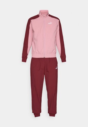 Puma trenirka z jopico na zadrgo, ki ima roza in burgundske sekcije ter ujemajoče se burgundske hlače. Material je lahek in gladke teksture.