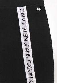 Černá elastická sukně s bílým bočním pruhem a textem "CALVIN KLEIN JEANS". Obsahuje malé vyšívané logo "ck" na pásku.