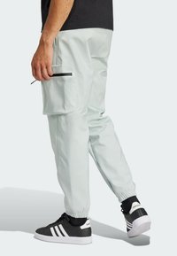 Lichtgrijze cargo pants met elastische cuffs, zijzakken en zwarte accenten. Dragen met zwarte sneakers met drie witte strepen.