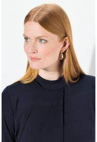 Tummansininen yläosa korkealla kauluksella ja laskostyksellä, yhdistettynä kultaisiin renkaisiin korvakoruihin. Sujuva pinta ja istuva muotoilu parantavat kokonaisilmettä.